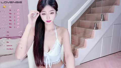 Media: Video of an East Asian woman with long, straight black hair, wearing a white lace bralette, posing indoors near a staircase.