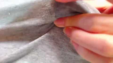 Media: A close-up video of a hand with light skin and short nails gently folding a soft, grey fabric, possibly a towel or blanket, with a textured, slightly rough surface.