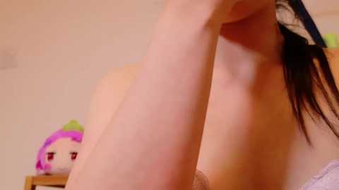 Media: Video of a woman with fair skin, wearing a white lace bra, adjusting her black hair. A plush toy with a pink face and green hat is visible in the background.