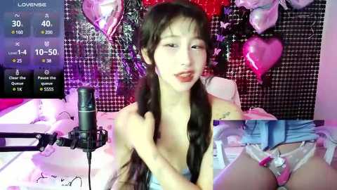 Media: Video of an Asian woman with long black hair in pigtails, wearing a white lace bra, posing seductively on a bed with pink heart decorations and a black grid background.