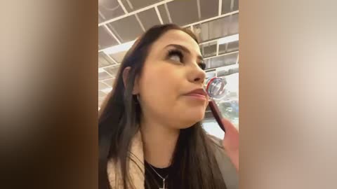 Media: A video of a young woman with long, dark hair, wearing a black top and a silver necklace, looking up through a magnifying glass, with a blurred background of a tiled ceiling.