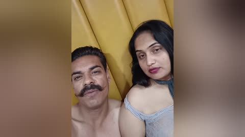 Media: Video of an Indian man and woman with light skin tones, the man with a mustache and the woman with dark hair, both smiling, against a mustard yellow backdrop.