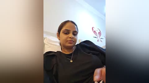 Media: Video of a Latina woman with medium skin tone, medium-length brown hair tied back, wearing a black smock, sitting in a salon chair with a white pillow behind her.