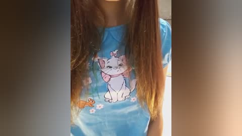 Media: A video of a young girl with long brown hair, wearing a blue T-shirt featuring a cartoon cat and a pink scarf. The background is blurry.