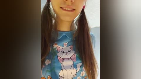 Media: A video of a young girl with long brown pigtails, smiling, wearing a blue shirt with a pink bow, featuring a cartoon cat in a hat.