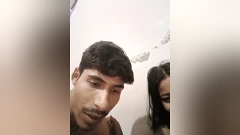 Media: A video of a young South Asian man with a mustache and a woman with long black hair, both partially blurred. They are indoors, likely in a bathroom with a white ceiling and shower head.