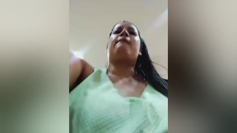 Media: Video of a middle-aged woman with a medium complexion and straight black hair, wearing a light green blouse, looking upward. The image is slightly blurred.