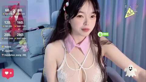 Media: A video of an Asian woman with long black hair, wearing a sheer, lace bralette and a pink choker, sitting on a grey chair.