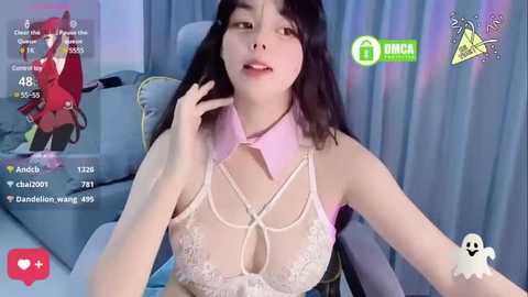 Media: Video of an East Asian woman with long black hair and fair skin, wearing a revealing, lace-up white crop top, seated in a modern chair. Background shows a room with a red character figure and a green logo.