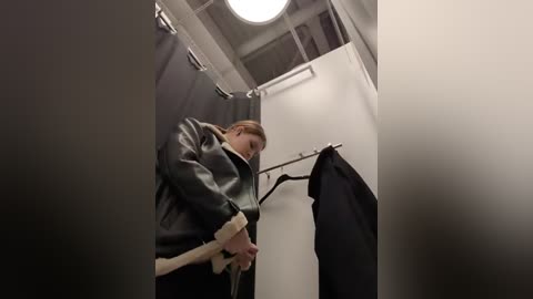 Media: A video of a person wearing a black leather jacket and holding a cane, standing in a dimly lit, narrow hallway with white walls and a metal railing.