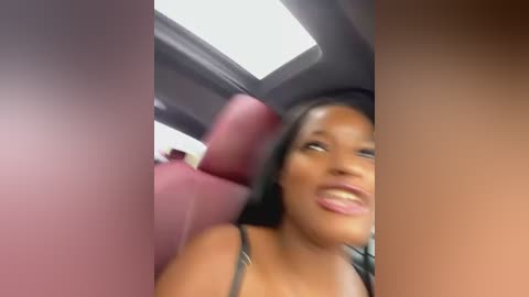 Media: Video of a young Black woman with long black hair, wearing a black top, smiling from the back seat of a car with pink interior.