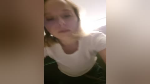 Media: A blurry, low-resolution video of a young woman with light skin, medium-length blonde hair, and a white t-shirt, seen from a close-up angle.