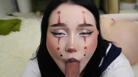 Media: Video of a pale-skinned woman with black hair, wearing a sailor uniform, performing oral sex on a man, her face painted with clown makeup, in a domestic setting.