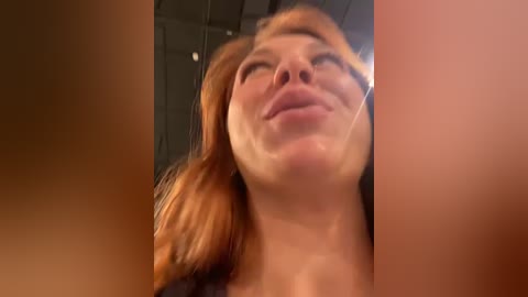 Media: Video of a young woman with reddish-brown hair and fair skin, smiling widely, captured from a low angle. Her eyes are closed, and her head is tilted back.