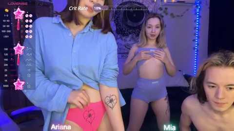 Media: Video of a young woman with short brown hair in a blue shirt, pink panties, and a spider tattoo on her arm, standing beside a topless woman covering her breasts with her hands.