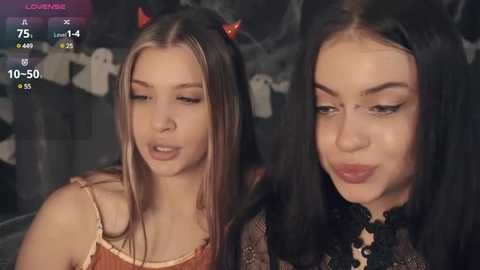 Media: Video of two young women with light skin, one with long blonde hair and red devil horns, the other with long black hair and dark makeup, both smiling.