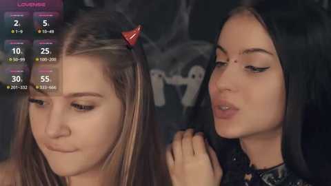 Media: Video of two young women, one with long brown hair in a ponytail, the other with long black hair, both wearing makeup, in a dimly lit room.