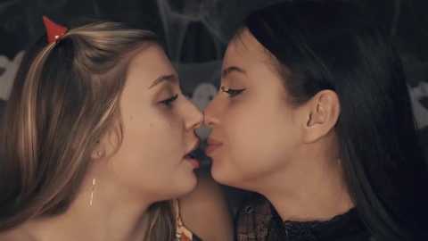 Media: Video of two young women, one with blonde hair and the other with black hair, kissing passionately in a dimly lit, intimate setting.