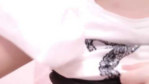 Media: Video of a woman's upper body in a white lace-trimmed blouse, partially unbuttoned, revealing a black bra. The background is blurred, emphasizing the delicate fabric textures.