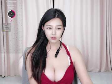 Media: A video of an East Asian woman with long black hair, wearing a revealing red bra and headset, seated indoors with beige curtains in the background.