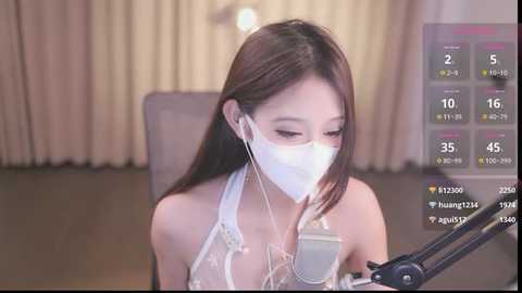 Media: Video of an East Asian woman with long brown hair, wearing a surgical mask and white halter top, singing into a microphone, surrounded by streaming app icons and temperature gauge.