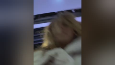 Media: Blurry video of a blonde woman in a white robe lying on a bed, with a muted, dimly lit background suggesting a bedroom.