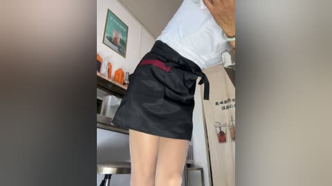 Media: A video of a woman in a white blouse and black skirt, leaning over a kitchen counter, with orange bowls and a framed picture on the wall in the background.