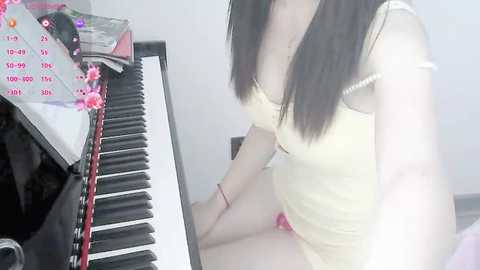 Media: Video of a woman with long black hair, seated at a piano, wearing a yellow tank top, and red panties.