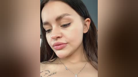 Media: Video of a young Latina woman with long black hair, light brown skin, and a tattoo on her shoulder, wearing a silver necklace. She has a soft smile and closed eyes.