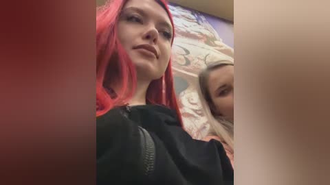 Media: A video of a young woman with bright red hair and fair skin lying on a bed, her face partially obscured by a blurred red filter. She wears a black hoodie and is next to a sleeping child.