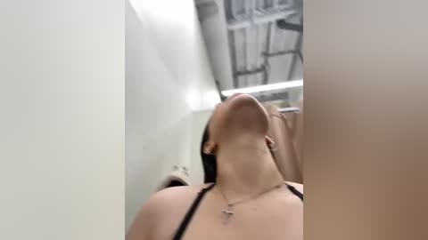 Media: A blurred video of a woman with long brown hair, wearing a black bra, leaning against a white wall in a narrow corridor, with an industrial ceiling visible in the background.