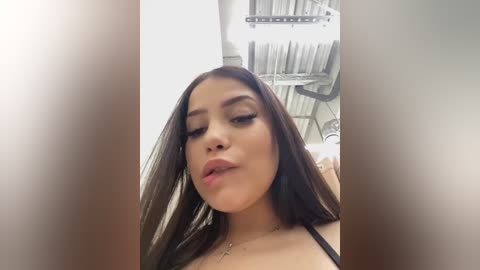 Media: Video of a Latina woman with long, straight brown hair, wearing a black bra, sitting on a dental chair. She has a medium complexion, full lips, and closed eyes. Background features a dental chair and dental tools.