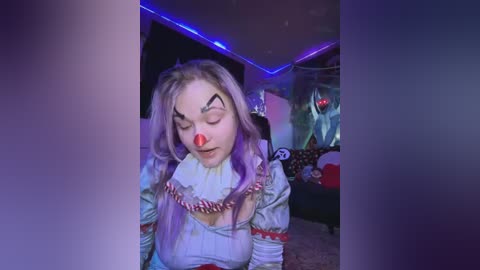 Media: Video of a young woman with light purple hair, wearing a white ruffled collar and red clown nose, with closed eyes, in a dimly lit room with purple LED strip lighting and a plush toy in the background.