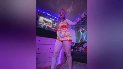 Media: A video of a curvy woman with red hair, wearing a colorful, anime-themed tank top and panties, dancing energetically in a dimly lit, cluttered bedroom.