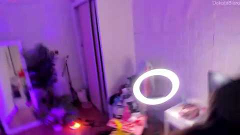 Media: A blurry video of a dimly lit bedroom with purple lighting, featuring a vanity mirror, scattered clothing, and a bed with a pink blanket.