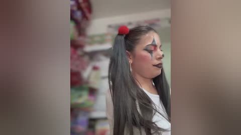 Media: A video of a young woman with long black hair in pigtails, adorned with red bows, wearing bold makeup, standing in a supermarket aisle with colorful products in the background.