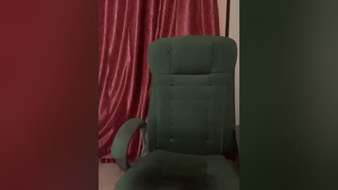 Media: Video of a teal, tufted armchair against a backdrop of red and green curtains. The chair has a high back, and the room appears dimly lit, emphasizing the textures and colors.