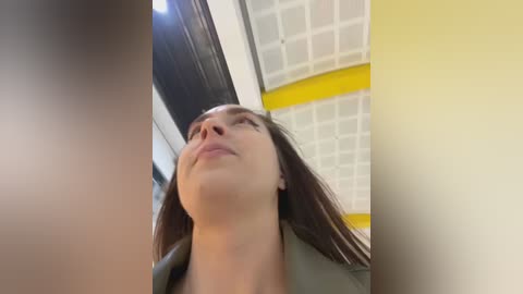 Media: A video of a young woman with long brown hair, light skin, and closed eyes, standing in a modern, brightly lit room with white ceiling tiles and yellow accents.