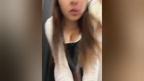 Media: A blurred video of a woman with long brown hair and a white top, possibly leaning over, with a dark background.