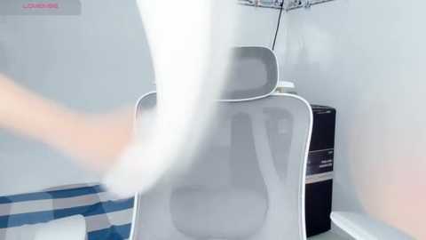 Media: Video of a white plastic chair with a see-through back, emitting a misty cloud, set against a white wall with a blue and white striped floor and a black filing cabinet in the background.