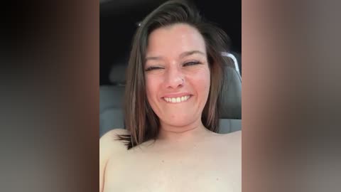 Media: Video of a smiling, light-skinned woman with shoulder-length brown hair, wearing a white top, sitting in a car.