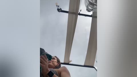 Media: A video captures a woman in a green top and black shorts, mid-air, wearing a black smartwatch, her eyes closed, floating near a white ceiling fan.