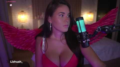 Media: A video of a young woman with long dark hair, wearing a revealing red top, holding a microphone, with large, red feathered wings.