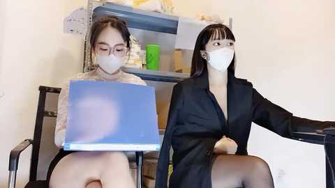 Media: Video of two Asian women wearing white masks, one in a sweater, the other in a black blazer, working at a laptop and a printer in a sterile office setting.