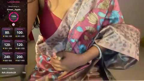 Media: Video of a person in a pink floral kimono with blue accents, holding a pink bra. Background shows a social media interface with green, blue, and red hearts, and a \"Love\" counter.