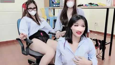 Media: Video of three Asian women in office attire, wearing white face masks, seated in a brightly lit room with desks and files in the background.