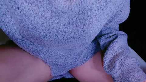 Media: Close-up video of a person wearing a light blue, textured sweater, revealing their bare thighs. The background is indistinct, with the focus on the fabric and skin.