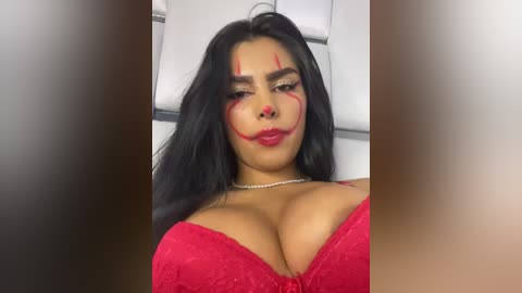 Media: Video of a curvy Latina woman with long black hair, wearing a red lace bra that accentuates her large breasts. She has bold red makeup and a silver necklace.