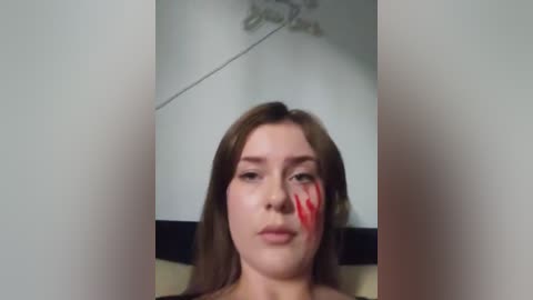 Media: A video of a young Caucasian woman with light skin, brown hair, and a red handprint on her face. She appears to be indoors with a ceiling fan visible.