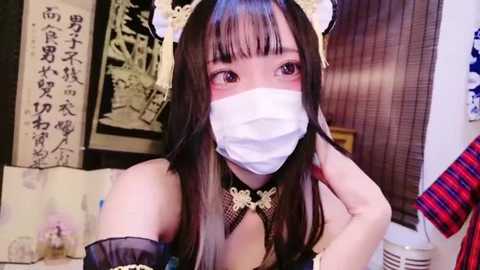 Media: Video of an Asian woman in a maid outfit with cat ears, wearing a white mask, blushing, in a cozy indoor setting.